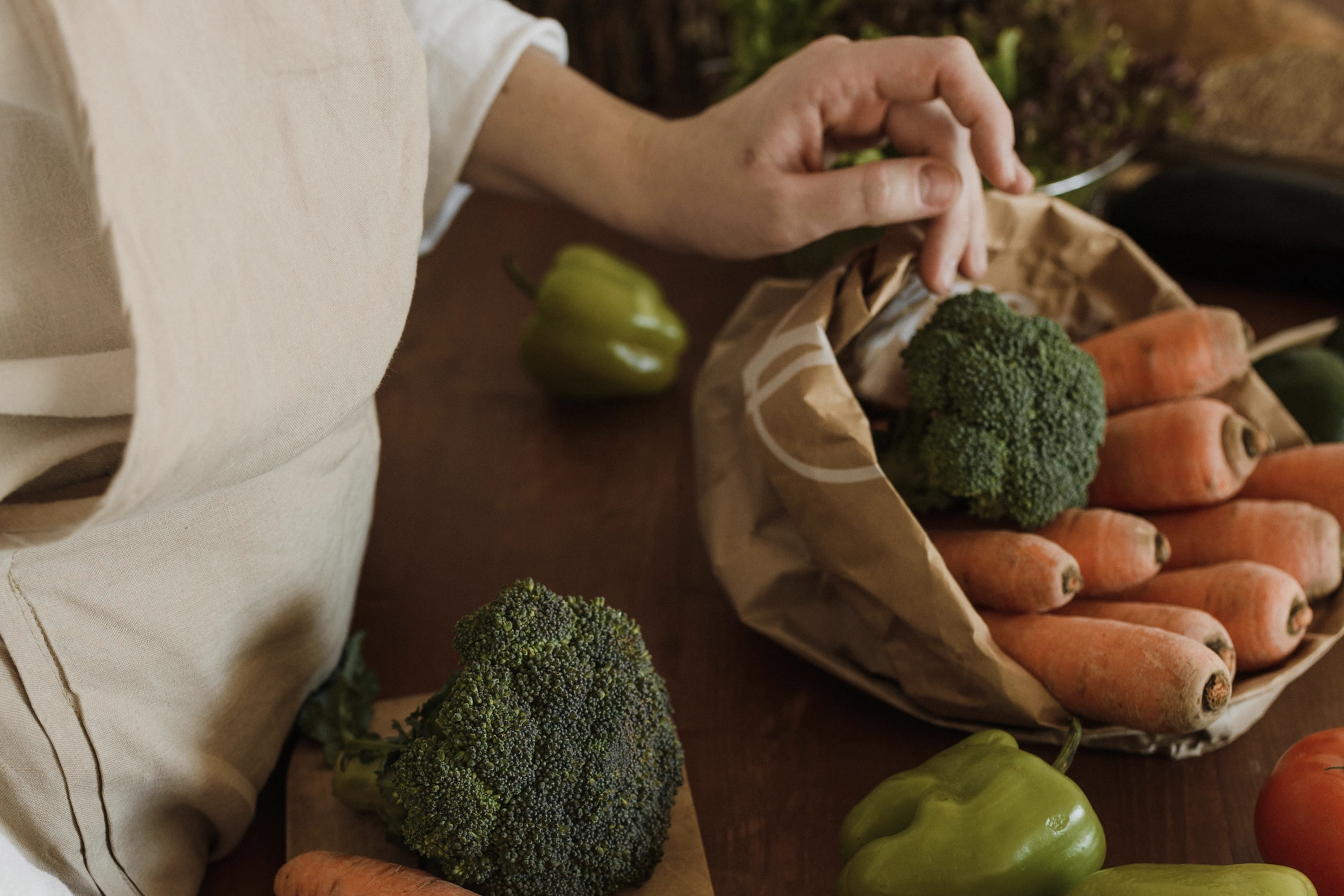 person facing paper bags filled with broccoli and carrots